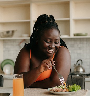 smiling woman at a kitchen island eating healthy foods