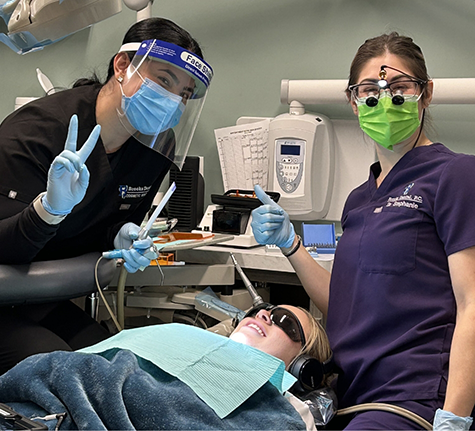 Two dentists giving a thumbs up next to a patient in the treatment chair