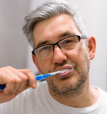 man with glasses brushing his teeth