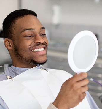 man looking at his new teeth in the mirror at the dentist’s office
