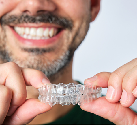 Smiling man holding two Invisalign clear aligners