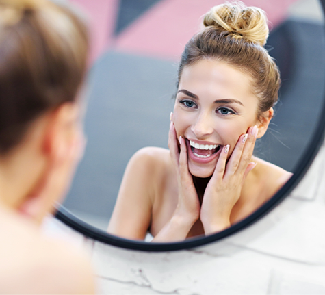 Woman smiling and touching her face while looking at her reflection