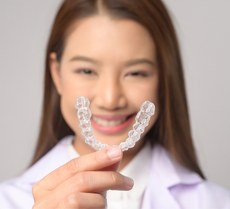 Smiling woman holding an Invisalign clear aligner