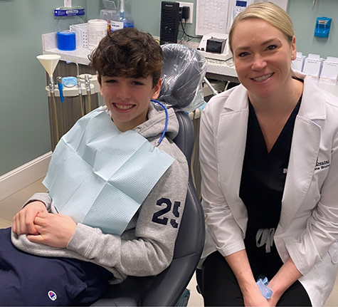 Orthodontist smiling next to a young man in the treatment chair