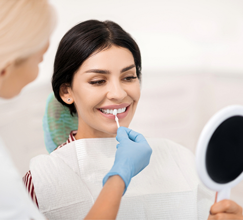 Woman smiling while a dentist holds a veneer to her tooth
